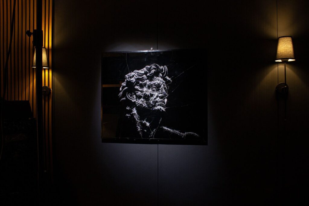 A broken glass portrait lit on a dark wall between two lamps
