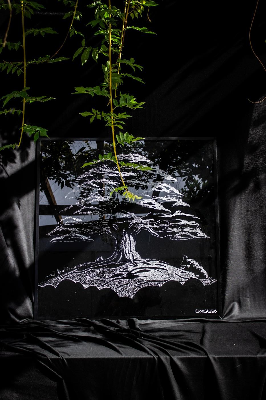 Un albero disegnato nel vetro rotto, fotografato tra le foglie